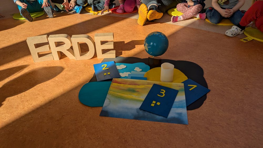 Kinder sitzen im Kreis vor einer kleinen Weltkugel und dem Wort ERDE aus Pappbuchstaben